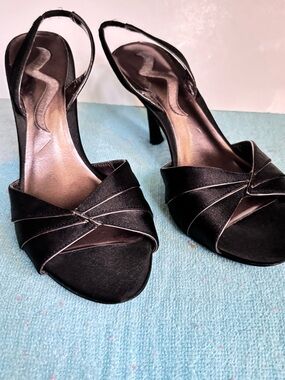 Nina black satin slingback heels feature a medium heel and silver trim